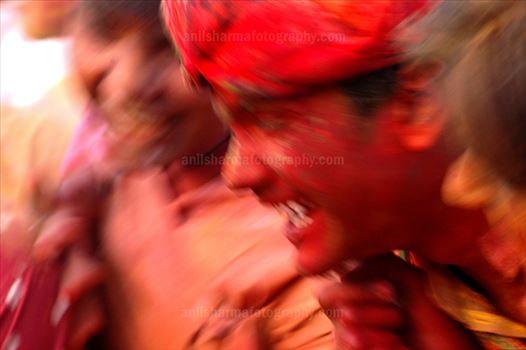 A man daubed in colored powder smiles as he celebrates Lathmaar Holi  at Nandgaon, Mathura, Uttar Pradesh, India.